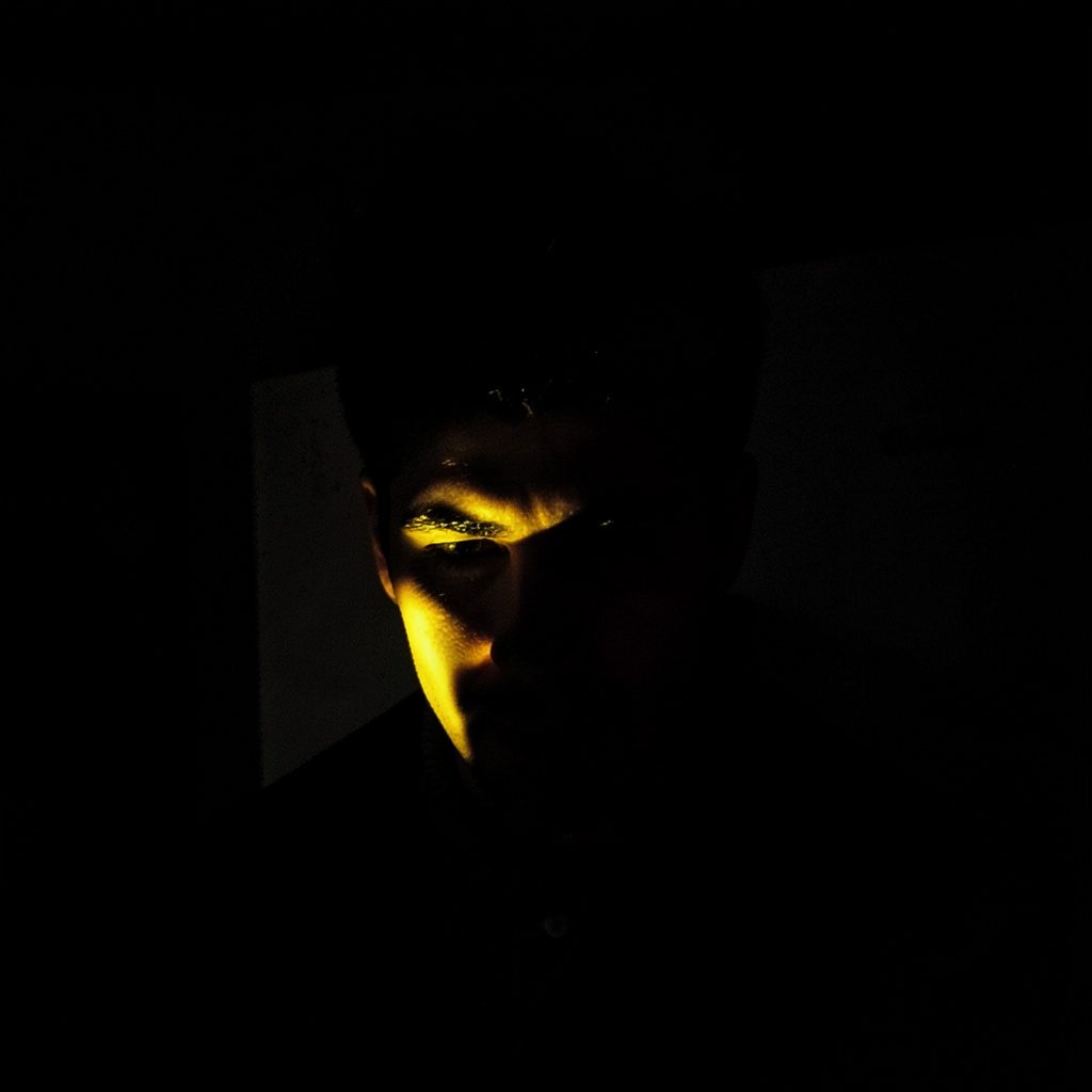 A dark, low-key photograph of deep amber and charcoal shadows, with soft golden rim light along the edges, evoking a dim, intimate mood